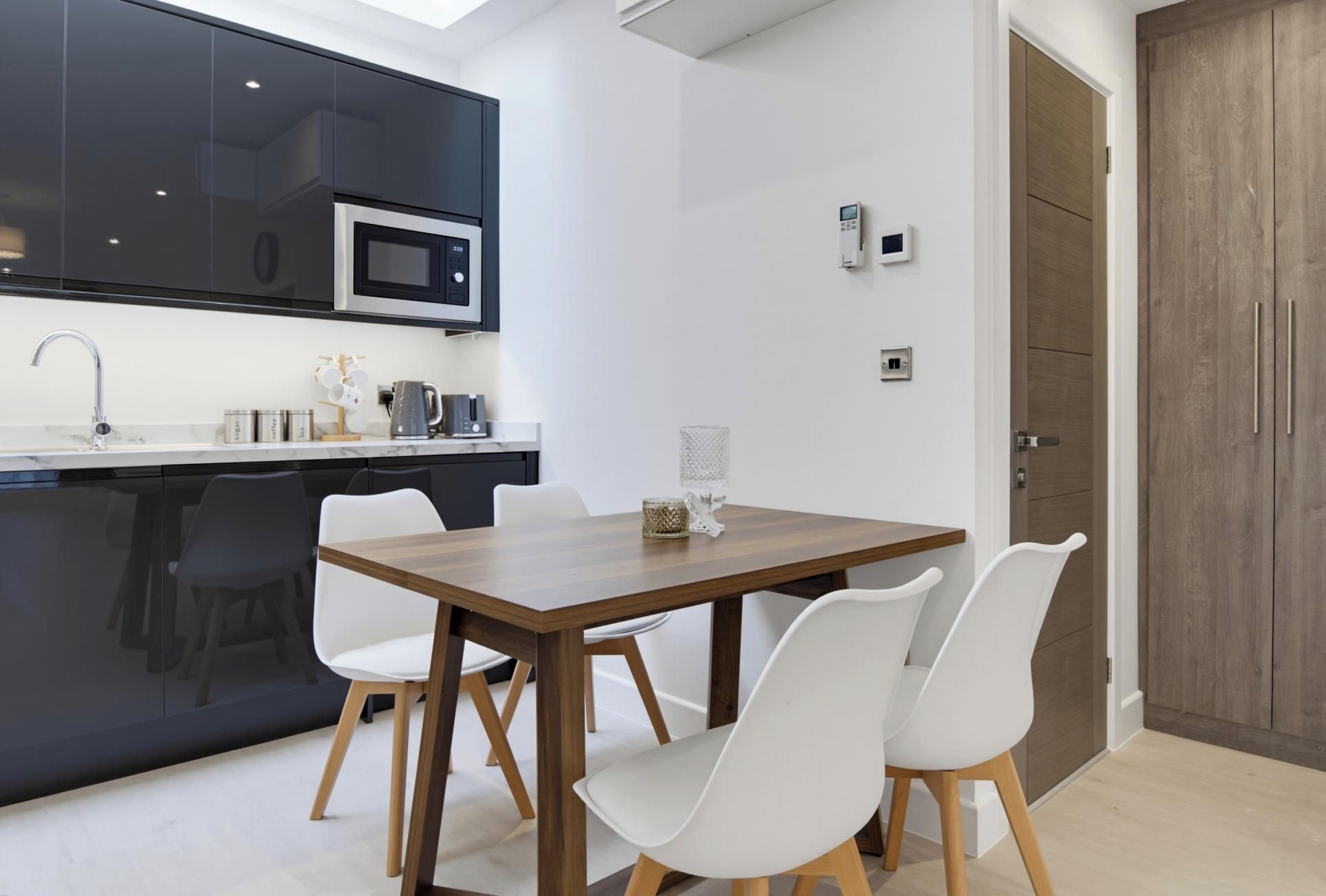 Une cuisine moderne équipée d’un four à micro-ondes, d’une machine à café et d’un coin repas avec une table en bois et des chaises blanches.