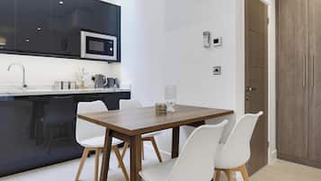 Une cuisine moderne équipée d’un four à micro-ondes, d’une machine à café et d’un coin repas avec une table en bois et des chaises blanches.