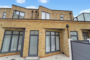 A two-story residential building with numbered doors, large windows, and a flat roof.