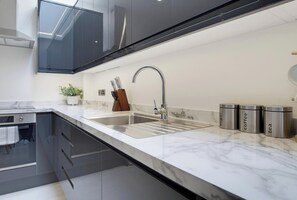 A modern kitchen with a stainless steel sink, a knife block, and three stainless steel containers labeled sugar, coffee, and tea.