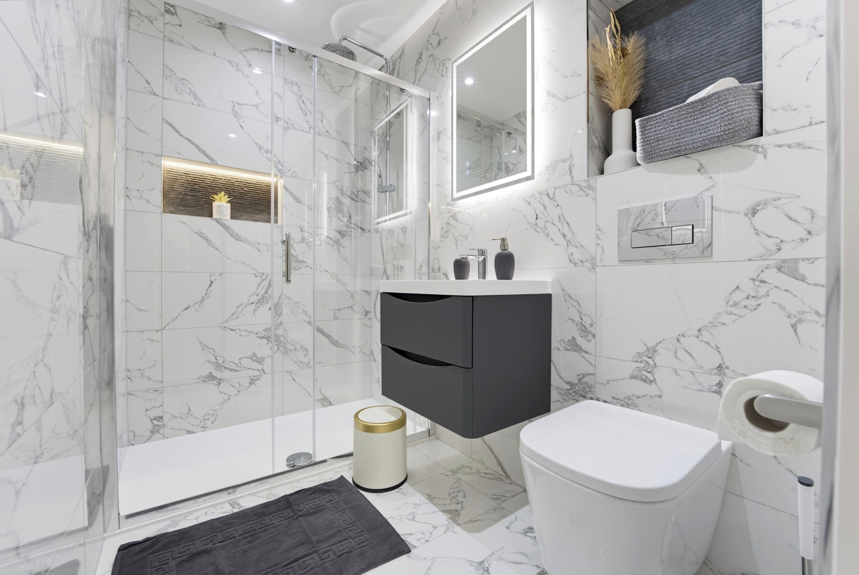 Un baño moderno con ducha envuelta en vidrio, inodoro blanco y pared con azulejos de mármol.