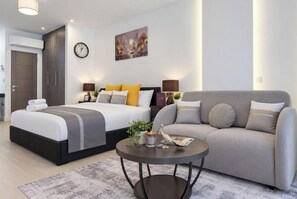 A modern hotel room with a double bed, a sofa, a coffee table, and a wall clock.