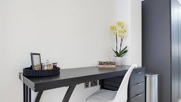 Un bureau moderne avec une chaise, une poubelle, un vase avec des fleurs jaunes et un tableau encadré posé sur le bureau.