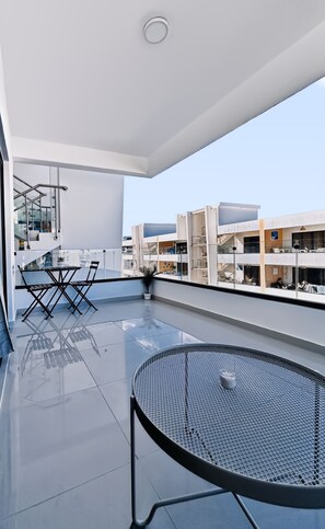 A modern balcony with a glass table and chairs, a potted plant, and a view of neighboring buildings. - The Reef · Pool & Home Cinema - Mins to Beach (Bayahíbe)