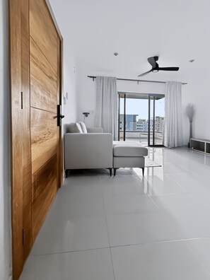 Een moderne woonkamer met een grote schuifdeur, een bank, een plafondventilator en uitzicht op de stad door een glazen deur.