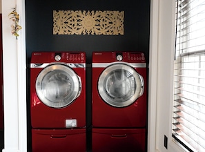 A pair of red Samsung front-loading washers installed in a laundry room with a decorative wall piece above them. - Cozy Fall Getaway in Broadripple (Indianapolis)