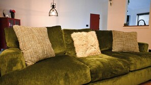 Un sofá verde de terciopelo con tres almohadas texturizadas y una lámpara colgante.