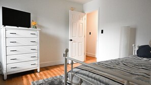 Un dormitorio con cama, cómoda, televisor y puerta que da a otra habitación.
