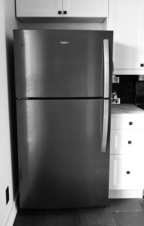 A stainless steel refrigerator with a double door, located in a kitchen with white cabinets and a tiled floor. - Cozy Fall Getaway in Broadripple (Indianapolis)