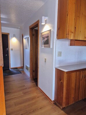 A hallway with wooden flooring, white walls, and wooden cabinets. There are light fixtures on the walls and a door at the end of the hallway. - Lovely 2-bedroom condo next to Teton Village/Skii Mountain Resort (Wilson)