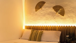 Cama bem arrumada com toalhas enroladas e um travesseiro, cabeceira de madeira e ventilador fixado na parede.