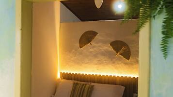 Quarto com cama, almofadas, ventoinha na parede e luminária no teto.