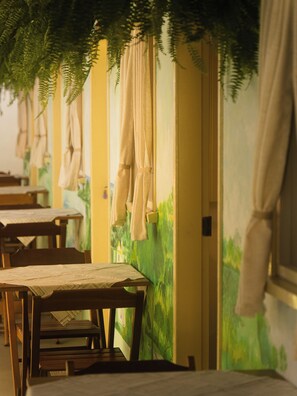 Ein Zimmer mit Holztischen und -stühlen, einer grünen Wandmalerei und hängenden Vorhängen.