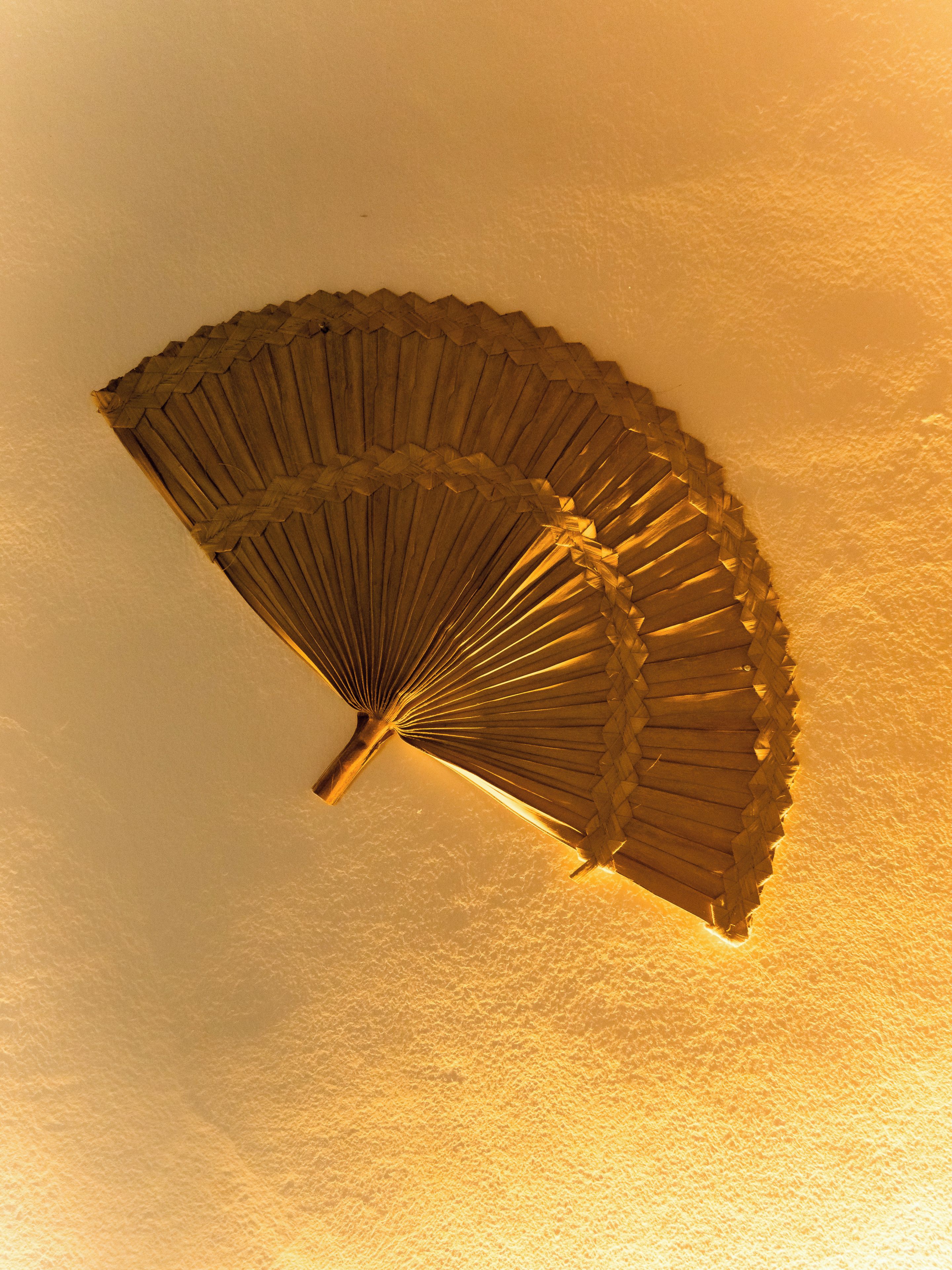 Ventilador de teto com design em madeira diante de uma parede lisa.
