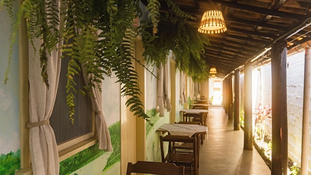 Um corredor com mesas e cadeiras, um lustre pendurado e uma parede com um mural de paisagem verde.