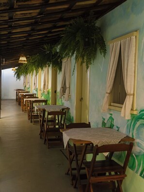 A row of wooden tables and chairs under a wooden ceiling with hanging plants.