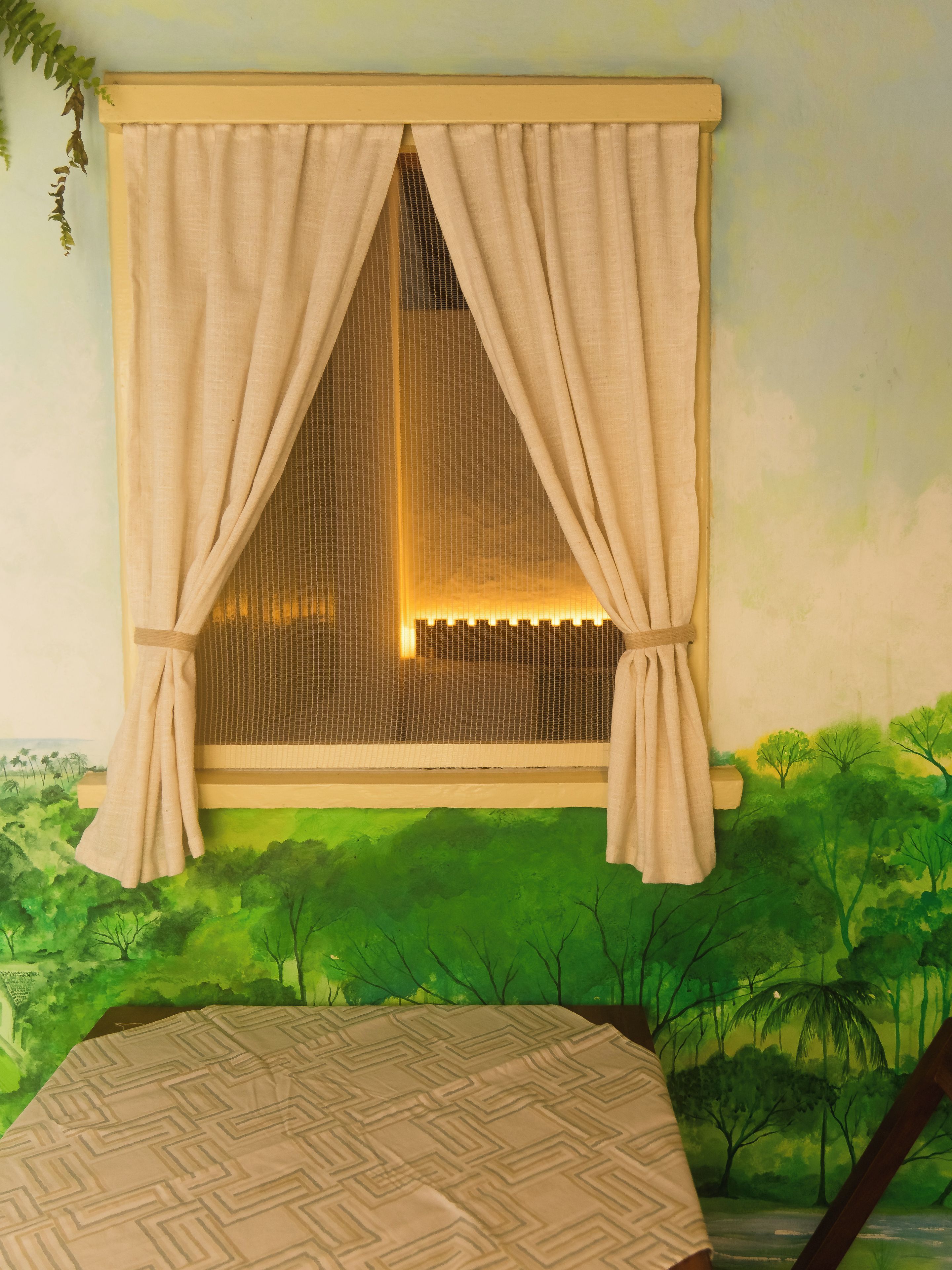 A room with a window, a bed, and a view of a green landscape.