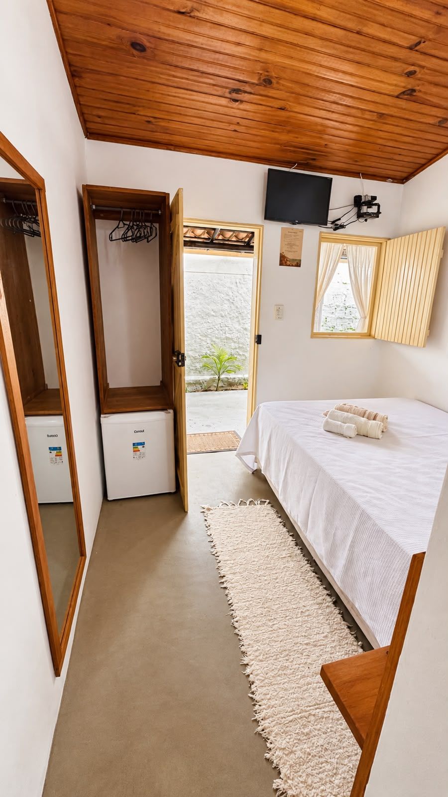 A bedroom with a bed, a wooden ceiling, a television, and a door leading outside.