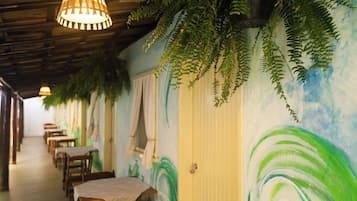A restaurant with wooden tables and chairs, hanging plants, and a mural on the wall.