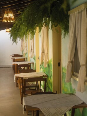A row of wooden tables with white tablecloths, a hanging light fixture, and a wall with a green mural. - Pousada Brisa Arraial (Porto Seguro)