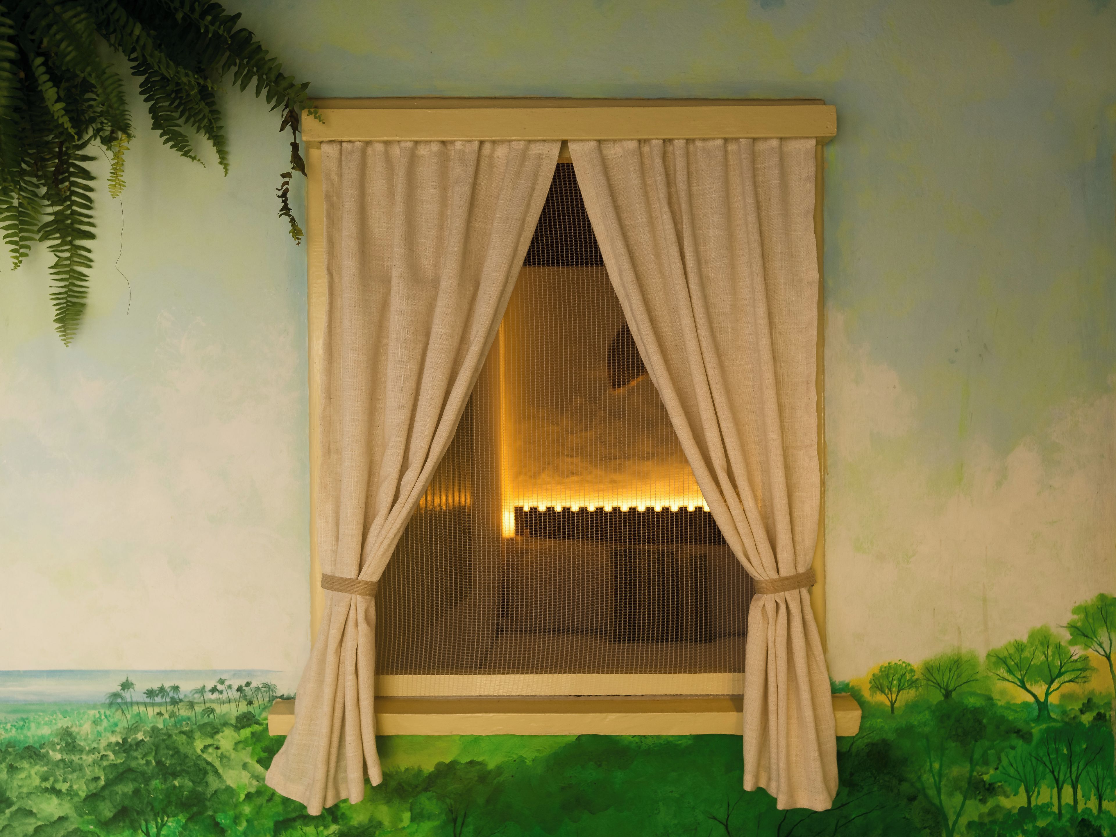 Una habitación con ventana, cortina, vista a un paisaje y un cuadro de árboles.