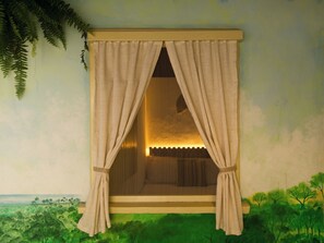 A room with a window featuring a curtain, a view of a landscape, and a painting of trees.