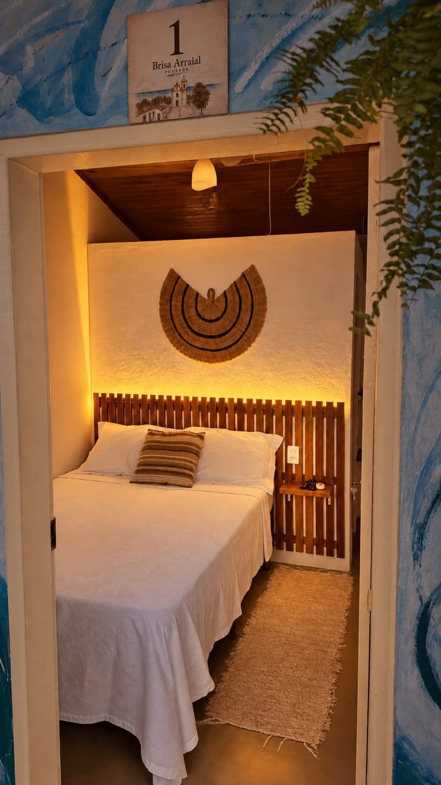Un dormitorio con cama, cabecera de madera, un adorno en la pared y un cartel sobre la cama.
