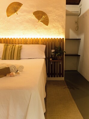 Habitación de hotel con cama, almohadas, mesita de noche con una planta y dos ventiladores de pared.