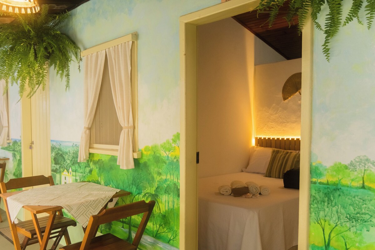 Ein Schlafzimmer mit einem Bett, einem Tisch, Stühlen und Blick auf eine Landschaftsmalerei.