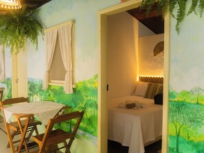 Ein Schlafzimmer mit einem Bett, einem Tisch, Stühlen und Blick auf eine Landschaftsmalerei.