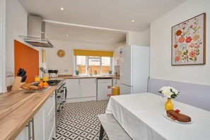 Eine kleine Küche mit Essbereich, ein Fenster mit gelben Jalousien und ein Wandbild mit Blumen.