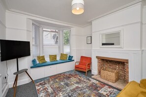 Ein Wohnzimmer mit Fernseher, Kamin, einer Bank mit Kissen und einem gemusterten Teppich.
