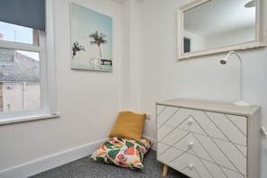 Ein Schlafzimmer mit einem Bett, einer Kommode, einem Fenster und einem Wandspiegel.