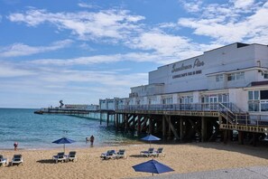 Un hôtel situé en bord de mer, doté d’une jetée qui s’avance dans l’eau, de chaises de plage et de parasols.