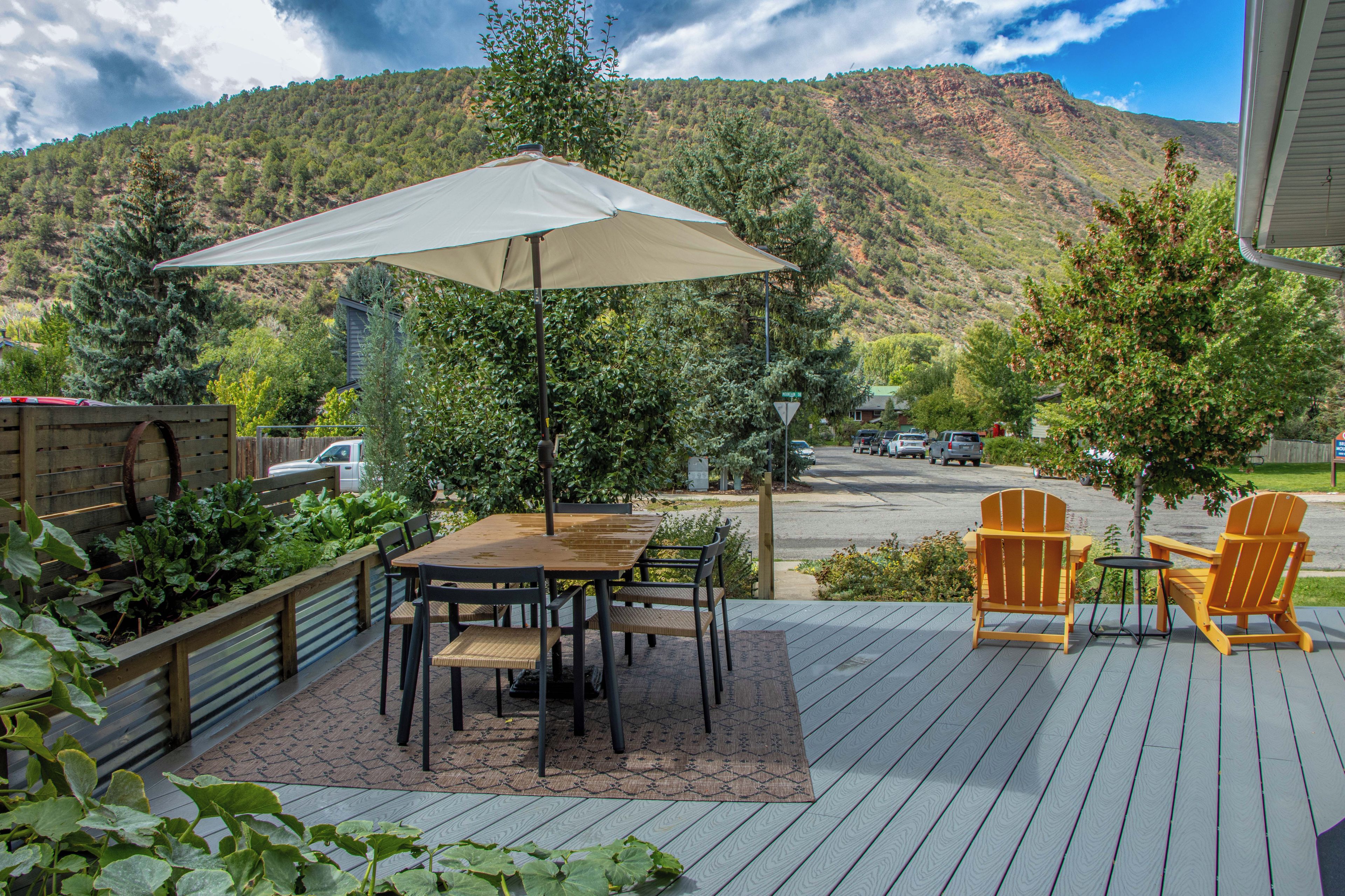 Una terraza con mesa y sillas, un gran paraguas y vistas a una montaña.