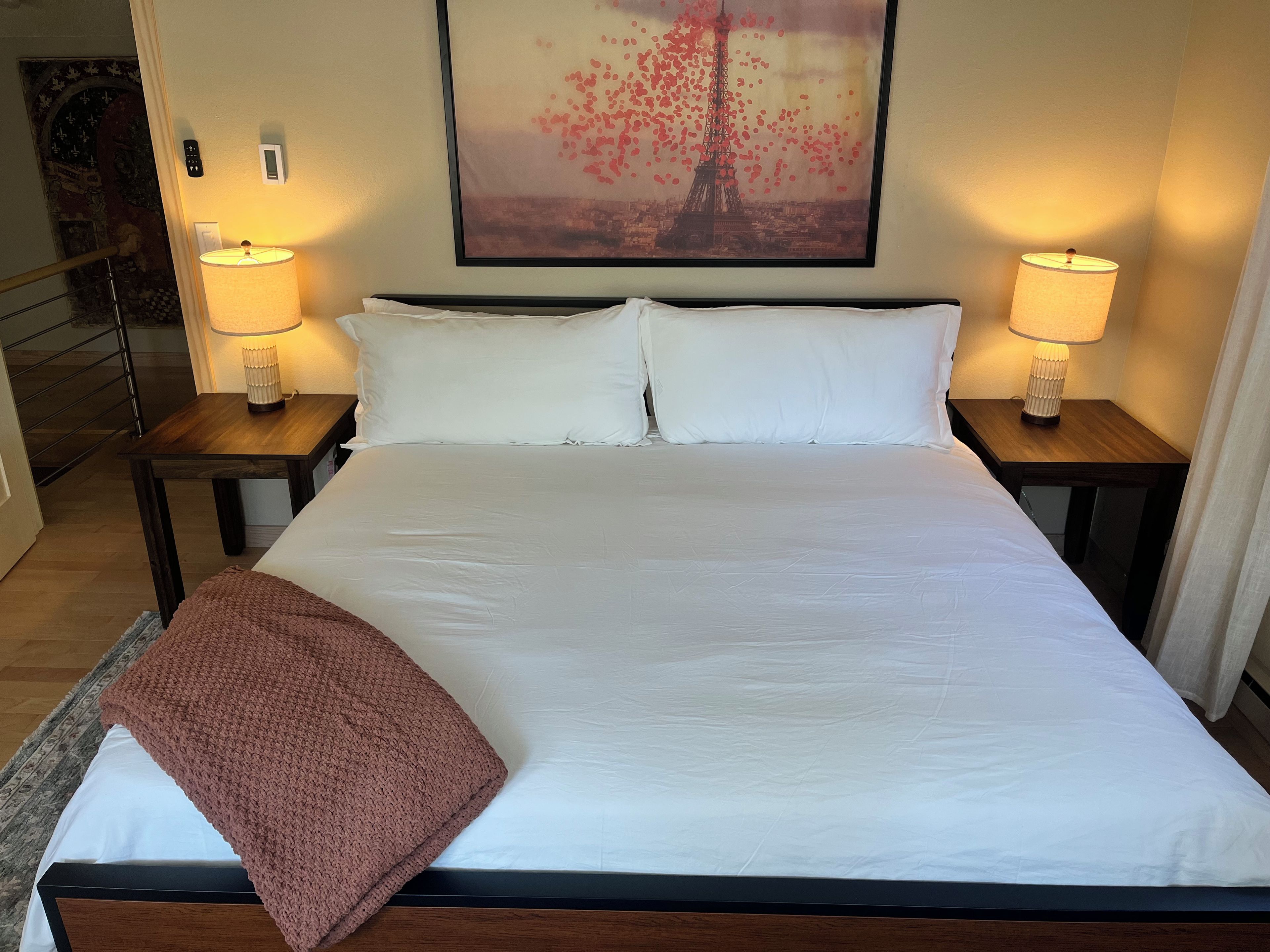Une chambre d’hôtel avec un grand lit, deux lampes de chevet, un tableau encadré représentant la Tour Eiffel et une tête de lit en bois.