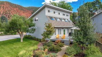 A two-story house with a covered porch, a lawn, and a mountain backdrop.
