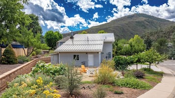 A single-story house with a metal roof, surrounded by a garden with various plants and a small patio area.