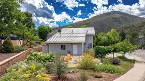 A single-story house with a metal roof, surrounded by a garden with various plants and a small patio area. - Garden Getaway Gardens, Canyon View, River Trail (Glenwood Springs)