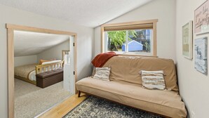 Um quarto aconchegante com sofá, janela com vista, porta que dá para outro cômodo e luminária no teto.