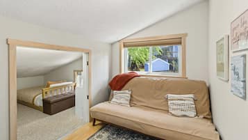 A cozy room with a sofa, a window with a view, a door leading to another room, and a ceiling light.