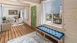 Interior de madeira com um banco, uma porta verde e vista para o exterior.