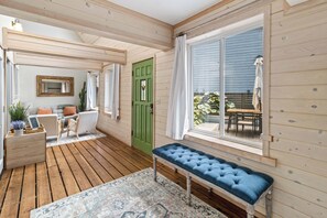 Interior de madera con un banco, una puerta verde y vistas al exterior.