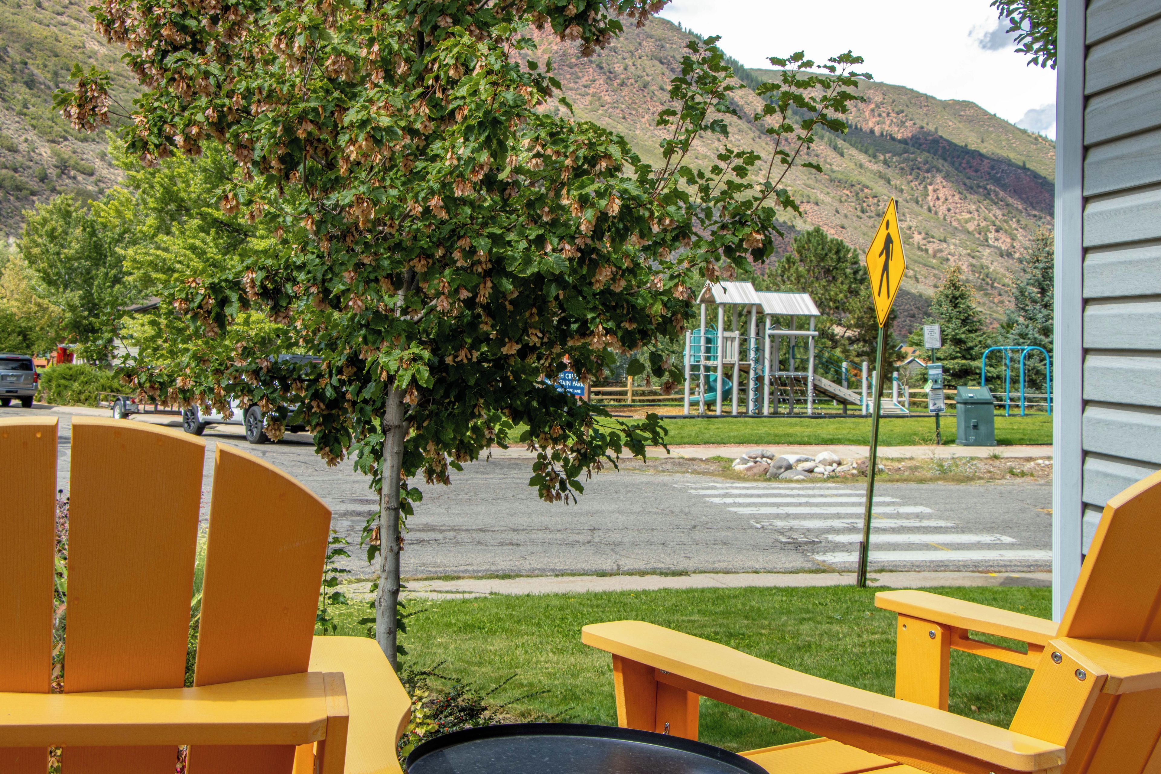 A view from a window overlooking a playground with a pedestrian crossing sign, a mountain in the background, and a parking area with vehicles.