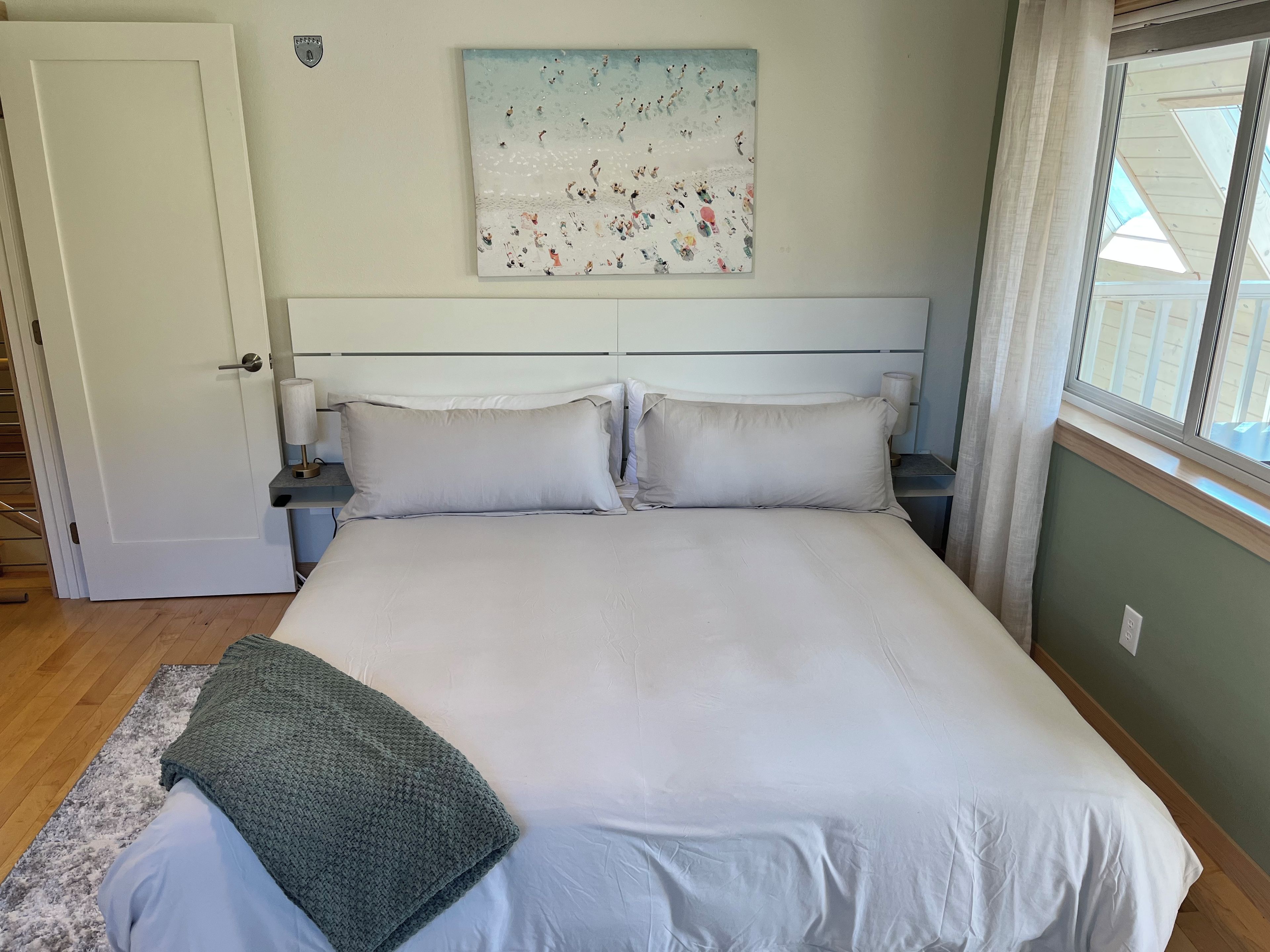 Une chambre à coucher avec un grand lit, deux tables de chevet, un tableau au mur et une fenêtre avec des rideaux.