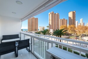 Ein Balkon mit weißer Reling, schwarzer Rattanmöbel und Blick auf hohe Gebäude und Palmen.