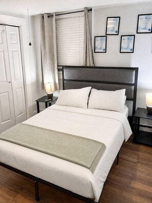 Een netjes opgemaakt bed met witte lakens, een donker hoofdbord en een nachtkastje met een lamp.