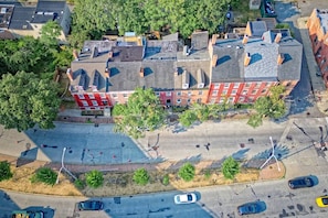 Luchtbeeld van een meerhoog gebouw met een rode bakstenen gevel, omgeven door bomen en een parkeerplaats.