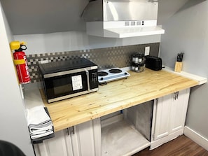 A compact kitchen with a microwave, stove, and a fire extinguisher.