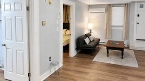 Ein Wohnzimmer mit einer Couch, einem Couchtisch und einer Lampe. Eine Tür führt in einen anderen Raum.